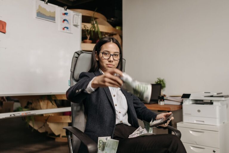 Confident businesswoman in eyeglasses counting dollar bills while sitting in a modern office.